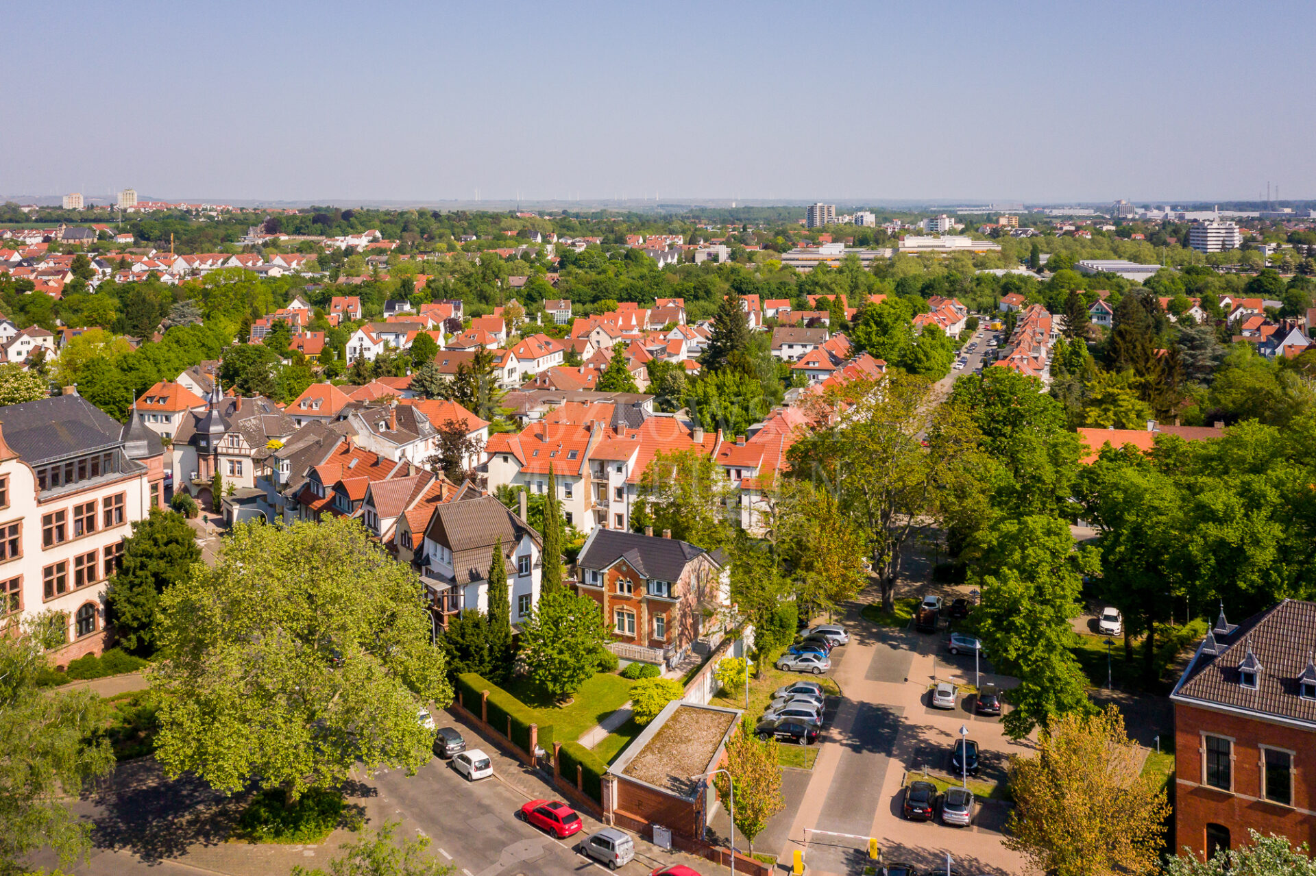 Luftaufnahme eines Vorortgebiets mit Häuserreihen, grünen Bäumen, die die Bodengesundheit unterstützen, und geparkten Autos unter einem klaren blauen Himmel.